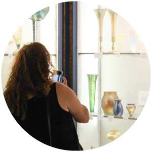 Woman taking a photo of the glass vases on display in the Museum of American Glass with her phone.