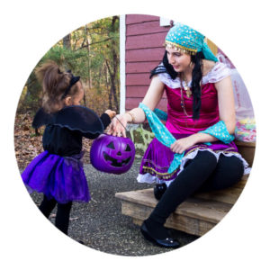 Woman dressed as a Romani person hands out halloween treats to a "bat-girl"