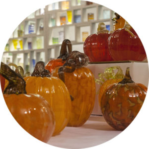 Circle crop of several orange glass pumpkins on display in the Studio Sale
