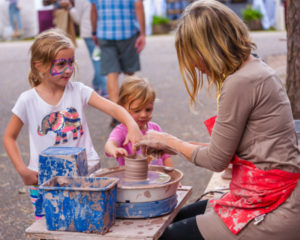 Two children touch clay being shaped by an artist at the potter's wheel during a demonstration at the Festival of Fine Craft.