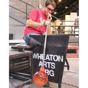 Artist blowing on blowpipe to manipulate glass piece