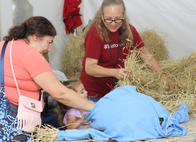 Two adults help a small child build a scarecrow at the Festival of Fine Craft at WheatonArts