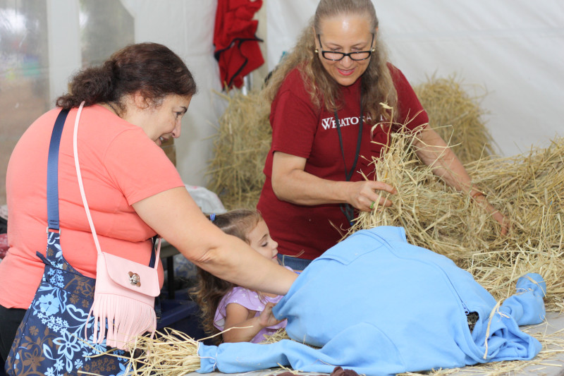 Two adults help a small child build a scarecrow at the Festival of Fine Craft at WheatonArts