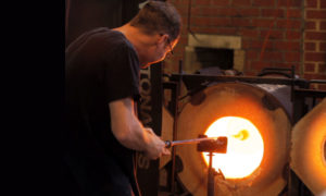 glassblower feeding glass piece into furnace