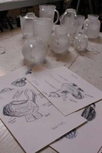 Sketches of glass pieces next to glass pieces laid out on table