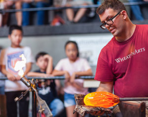 Glass Studio Artist Skitch Manion shaping glass in front of an observant audience