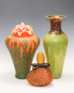 Flower top urn with leaves up the body, a green vase, and a glass Cairn, by artists Melanie Guernsey Leppla and David Leppla.