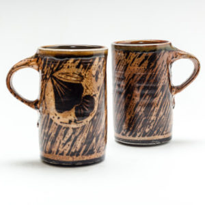 Tall tan mugs decorated with black stripes and flowers. Created by Terry Plasket