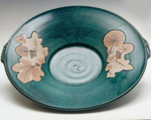 Green ceramic bowl decorated with pressed leaf designs on a tan background. Created by Amy Peseller