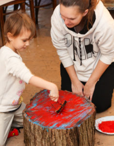 Child rolling red ink onto the rings of pre-cut log, the first step to create a Tree Ring Print.