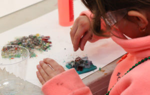 A young girl creating a magnet with glue and glass frit to be fused together later in the kiln.