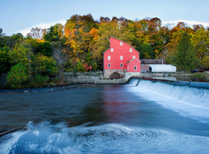 Photograph taken by James Evangelista of a red water mill house across from a large body of swirling water with a small waterfall.