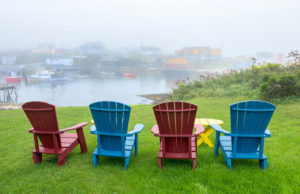 Photograph taken by James Evangelista of four Adirondack chairs on lush green grass, overlooking a foggy river.