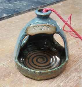 A small blue birdhouse feeder with a small sign that says enjoy on the top created by WheatonArts Ceramic Artist Tessa Carlton.