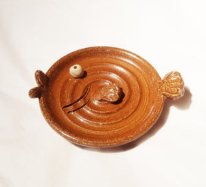 Brown circular dish with lips, a tail, a fin, and a white eye like a fish.