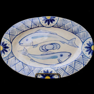 two circling fish painted with blue lines with decorative pattern around rim of a ceramic plate.