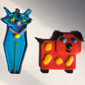 a sad Blue cat with yellow eyes and a happy red dog with yellow spots, blue eyes, and black feet, ears, and tail, both made from fused glass