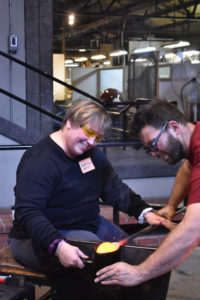 Instructor Skitch Manion teaches a woman how to shape hot glass in the Glassblowing Intensive class.