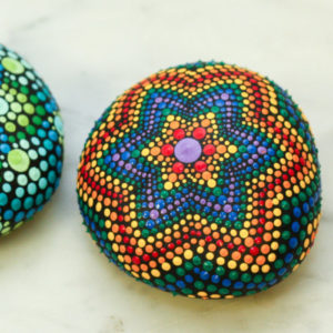 A rock with a dotted mandala painted with a rainbow of colors.