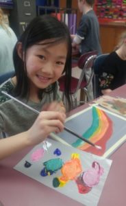 Smiling girl painting a rainbow in classroom