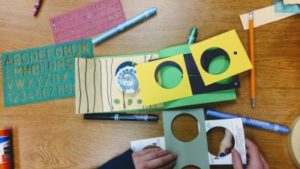 Overhead shot of hands working with construction paper and markers on a wooden table