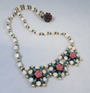 Necklace of various green, white, yellow, and pink beads, arranged in a floral pattern with a brass colored flower link.