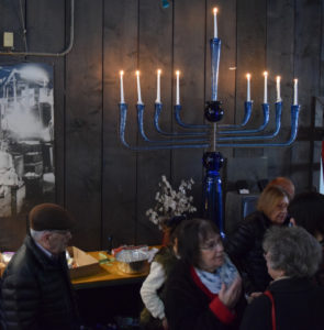 A 5'7" lit up blue glass menorah on a table, behind a group of visitors