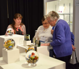 Three women viewing paperweights on display.