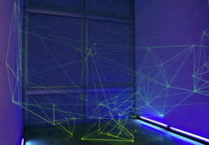 Installation of refracting green lights creating complex lines in a blue room with purple lights. Created by Evan Voelbel.