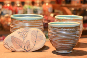 Ceramics by Amy Peseller. Three green and brown striped ceramic cups and one brown fired piece of clay decorated with pressed leaves.