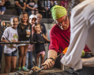 a family watches as Glass Artist Joe M. molds glass in the studio.