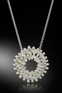 Silver necklace with pendant of two bright silver rings with small diamonds all the way around. Created by Isabelle Ecker.