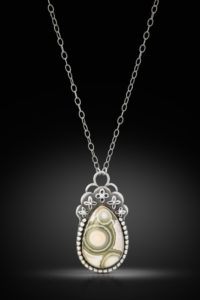 Silver necklace with ovate yellow and green gemstone pendant with circle and floral embellishments. Created by Janine Krantz.