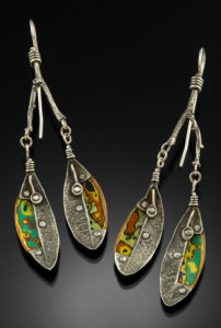 Each silver earring is shaped like a twig with two leaves, decorated with rivets and markings. Created by Logan Louis.