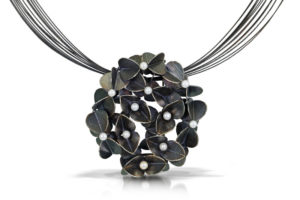 Strings connect to a pendant of iridescent metal flowers with a small bead in each center. Created by Christine Mackellar.