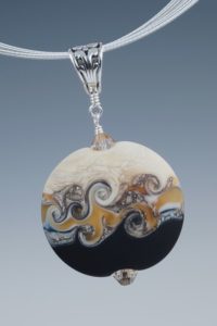 Oval pendant with waves of tan and white between a crackled white top and deep blue bottom. Created by Elizabeth Mitchell.