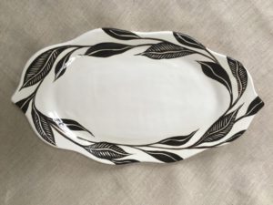 White wavy oval serving plate tapered at each end, decorated with painted black leaves. Created by Dorrie Papademetriou.