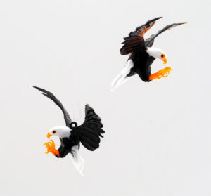 Small, intricately sculpted glass bald eagles with talons extended and wings outstretched, created by artist Thomas Von Koch