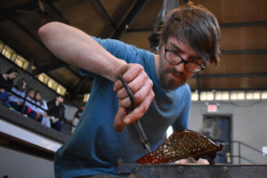 Closeup of WheatonArts Glass Artist Brian R. sculpting a glass wing. Spectators watch in seats from above.