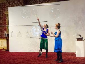 Artists Martha McDonald and Laura Baird play clear glass gongs with small circle mallets in the Museum of American Glass