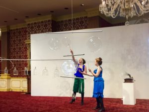 Artists Martha McDonald and Laura Baird play clear glass gongs with small circle mallets in the Museum of American Glass