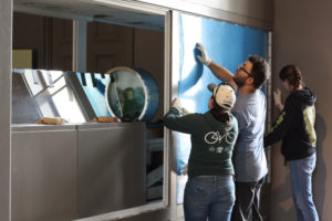 Glass studio manager Skitch Manion and studio assistants Lisa and Patty, as they put up the side panels around the ball mill motor and drum.