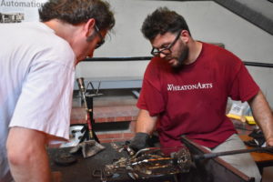 WheatonArts Glass Studio Artist Skitch Manion and "Emanation 2019" Artist Tristin Lowe plan placement of clear glass limbs on the large clear glass bottle.