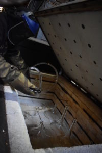 Closeup of hands covered in protective gear placing various glass funnels and tubing into a large box.