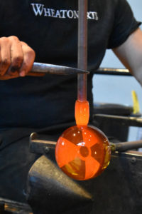 Closeup of hands using tweezers to create a uranium glass orb with a 'Hazardous' symbol.