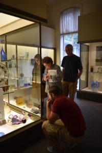 Director of Exhibitions and Collections Kristin Qualls, "Emanation 2019" Curator, Julie Courtney, Emanation 2019 Artist Jesse Krimes, and Hank Adams look at a display of various glass pieces in the Museum of American Glass