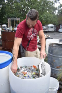 Emanation 2019 Artist Jesse Krimes reaching into a large, round white bin full of broken glass pieces.