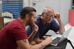 Hank Adams and Emanation 2019 Artist Jesse Krimes bending in to look at a laptop in the Glass Studio.