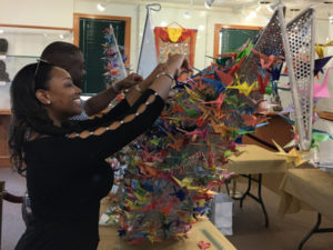 Two people attach origami cranes to the special "one thousand cranes" installation in the Down Jersey Folklife Center