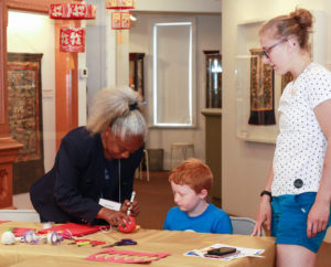 WheatonArts staff member Rosa assists a child and an adult creating paper lanterns in the Down Jersey Folklife Center at WheatonArts